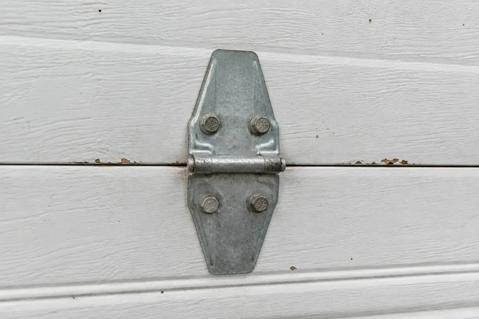 Metal center hinge across a seam in a white sectional garage door. — Garage Door Hinge Replacement, London