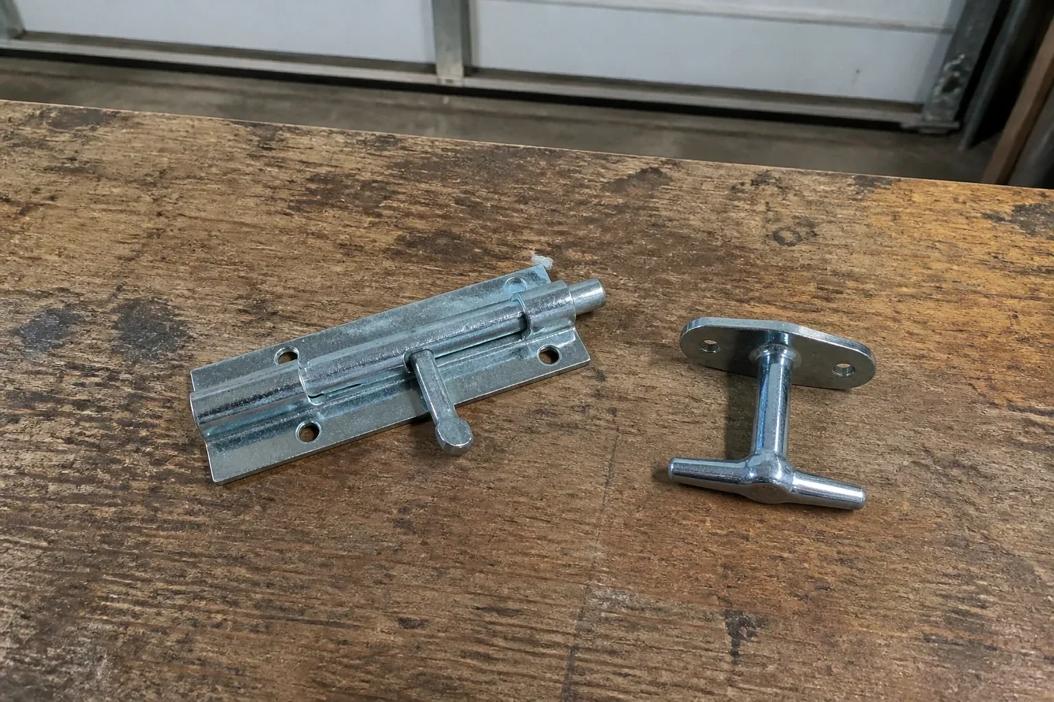 Detached slide bolt and T-handle on a wooden garage workbench. — Garage Door Manual Lock Repair, London